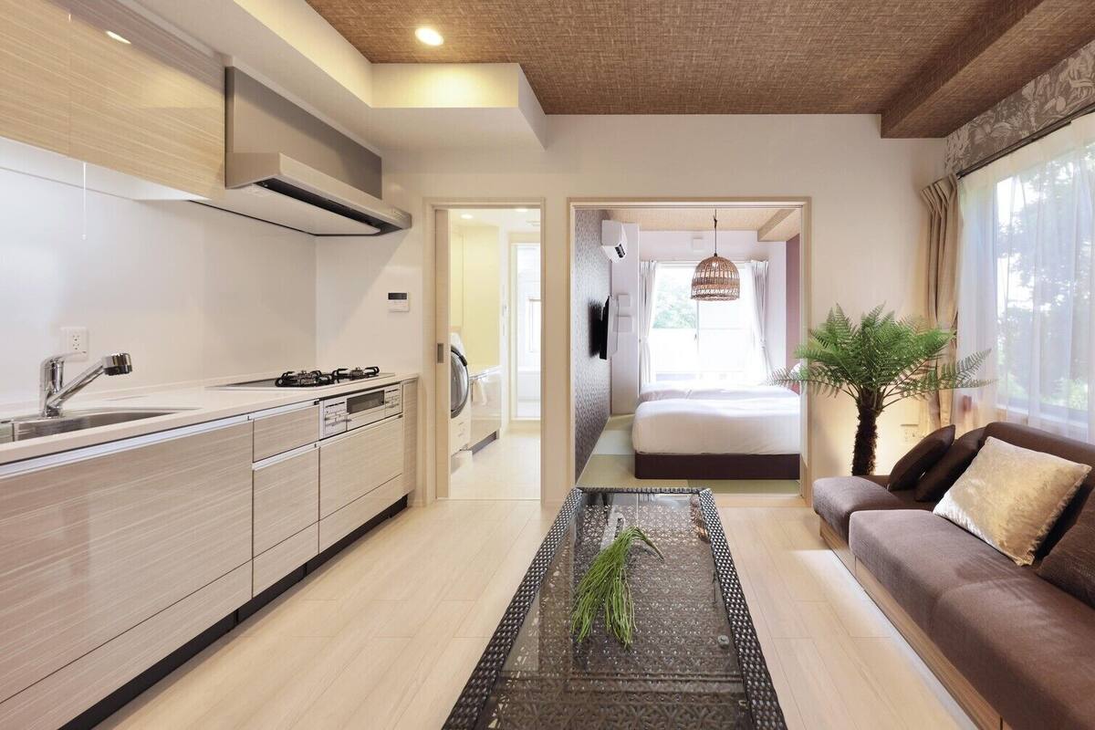 Une cuisine moderne avec un îlot central, un coin repas avec un canapé et une chambre avec un lit et une fenêtre.