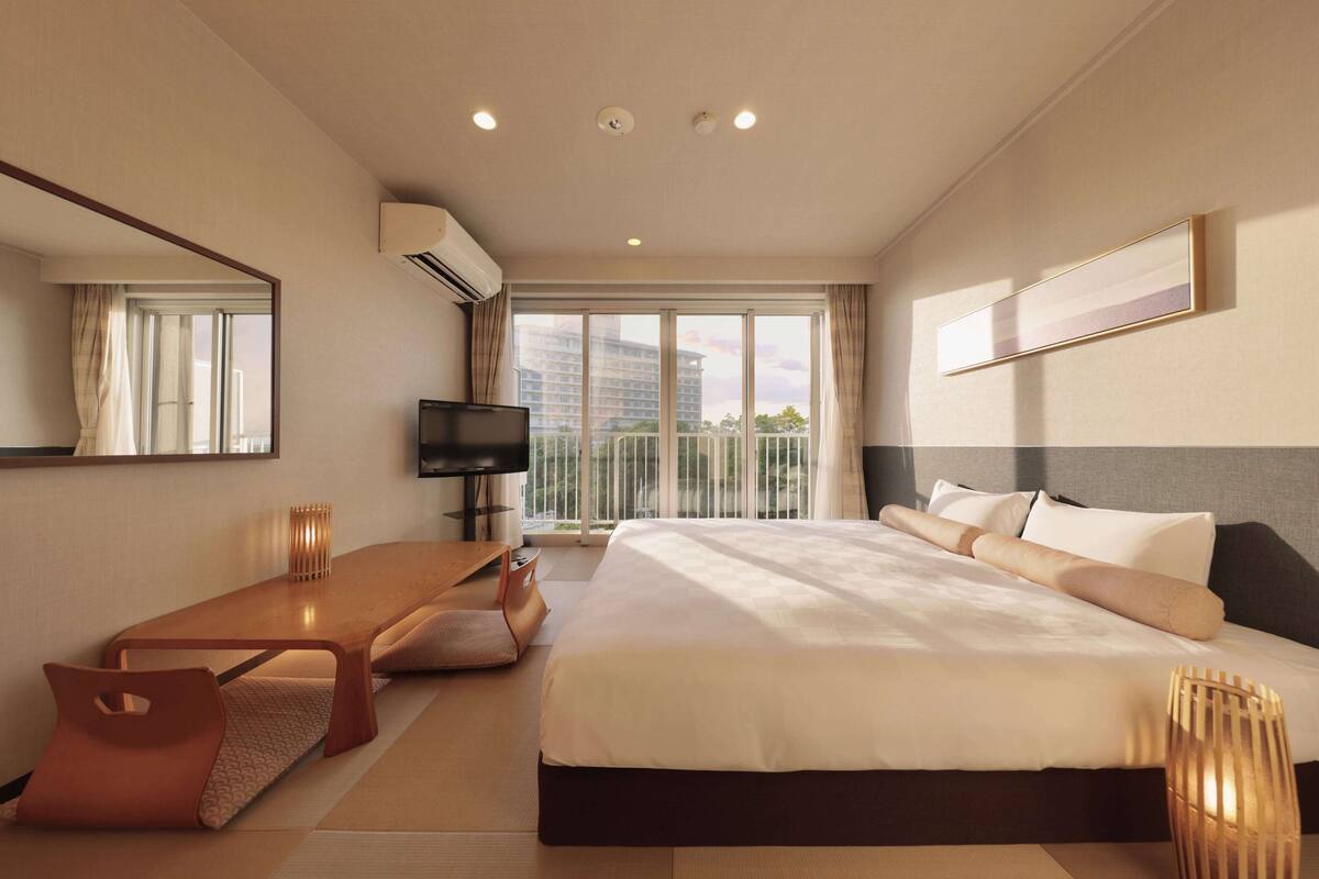 Une chambre d’hôtel moderne dotée d’un grand lit, d’un bureau, d’une télévision et d’un balcon offrant une vue sur la ville.