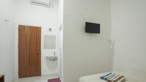 Una camera da letto con un letto, una televisione a muro, una porta in legno, un lavandino e un tappeto piccolo.