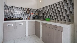 A kitchen with a tiled backsplash, a stove, and cabinets. - Sakura Guest House (Palembang)