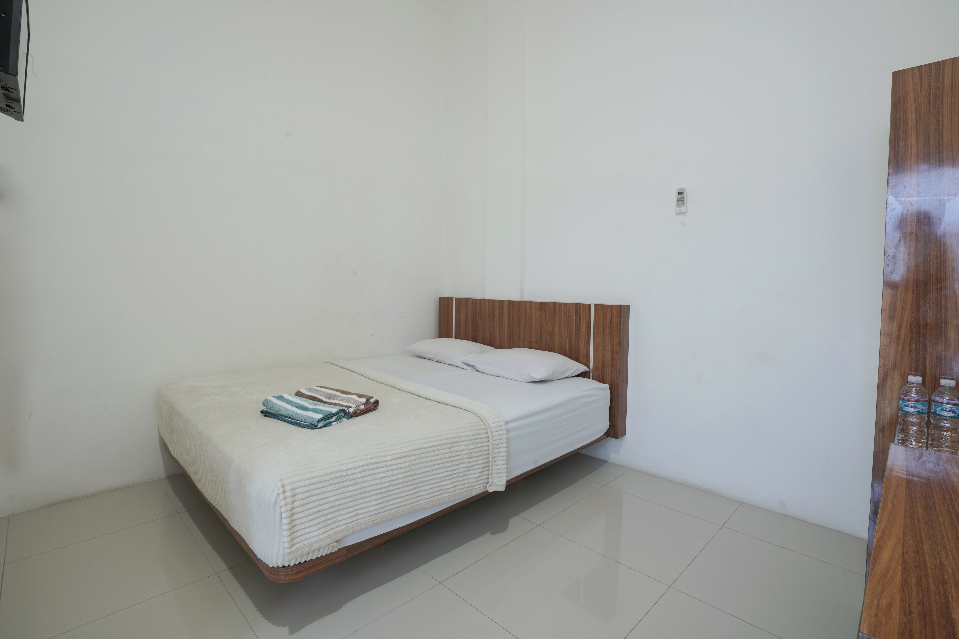 A small, clean room with a single bed, a wooden headboard, and a wooden wardrobe.