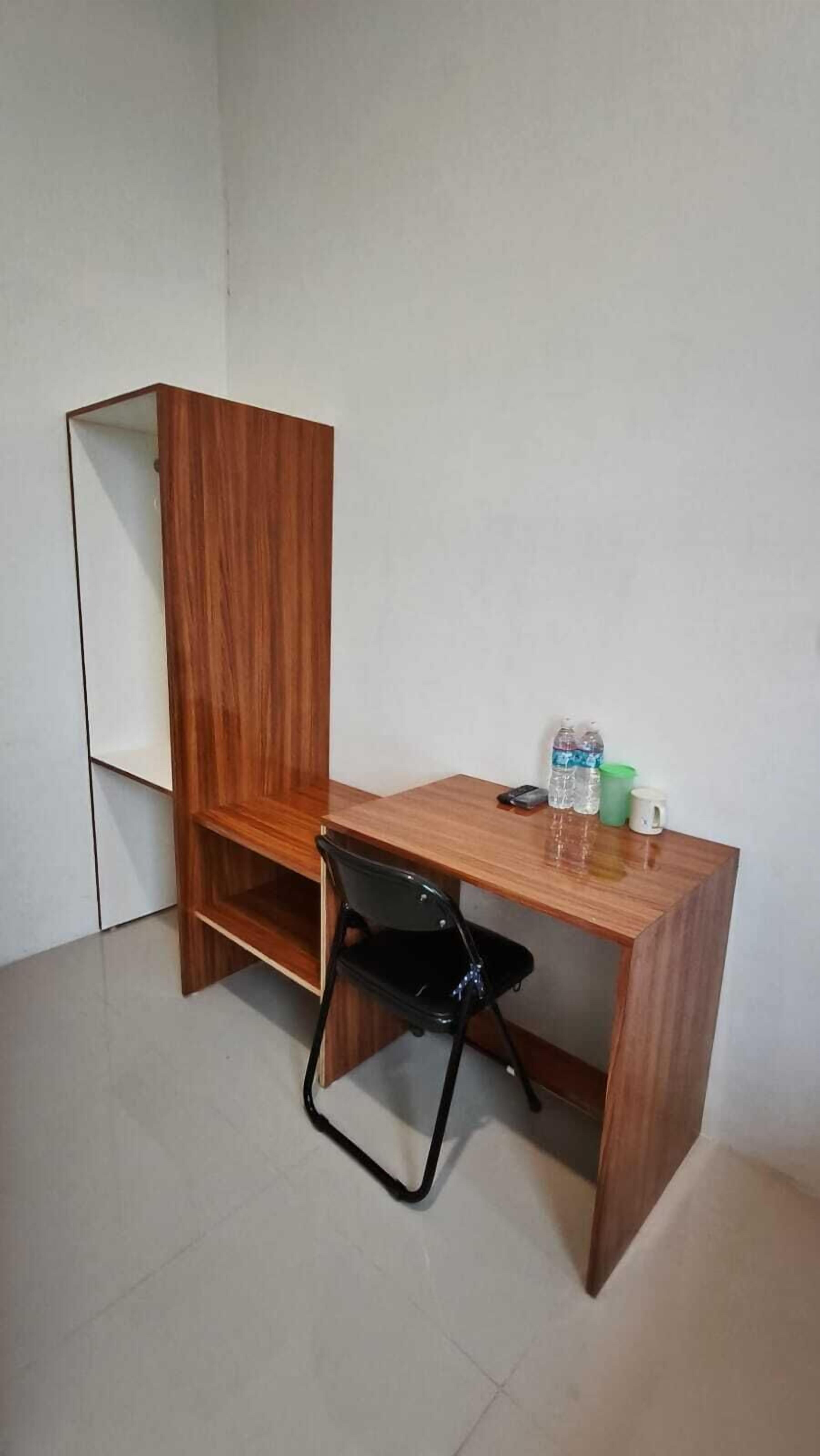 A small, wooden desk with a black chair, a water bottle, and a mug on it.