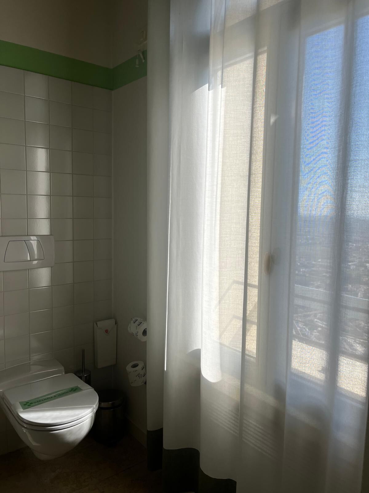A bathroom with a toilet, a trash bin, and a shower curtain.