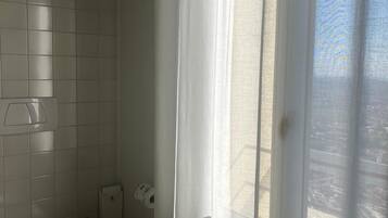 A bathroom with a toilet, a trash bin, and a shower curtain.