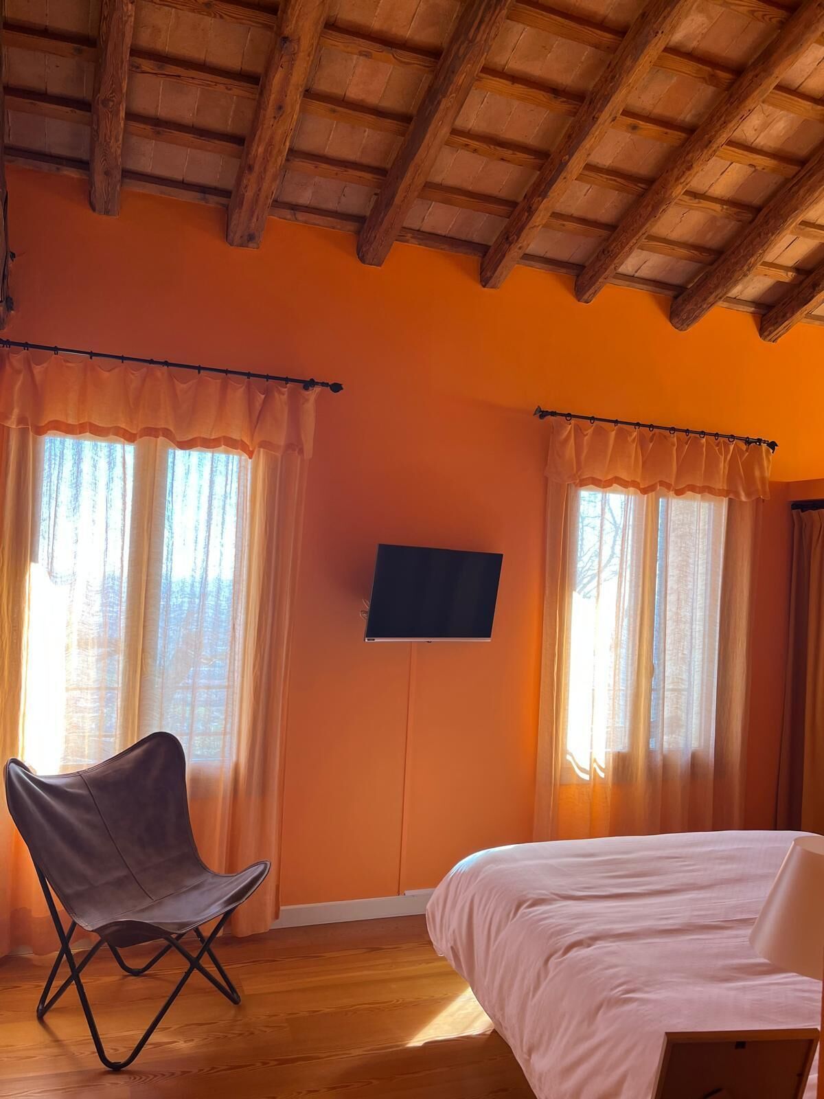 A room with wooden beams on the ceiling, a bed, a chair, and a TV mounted on the wall.