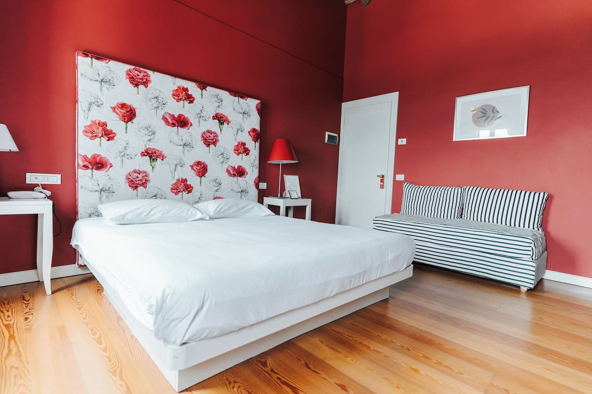 Een slaapkamer met een groot bed, een nachtkastje, een lamp, een gestreepte bank en een deur.