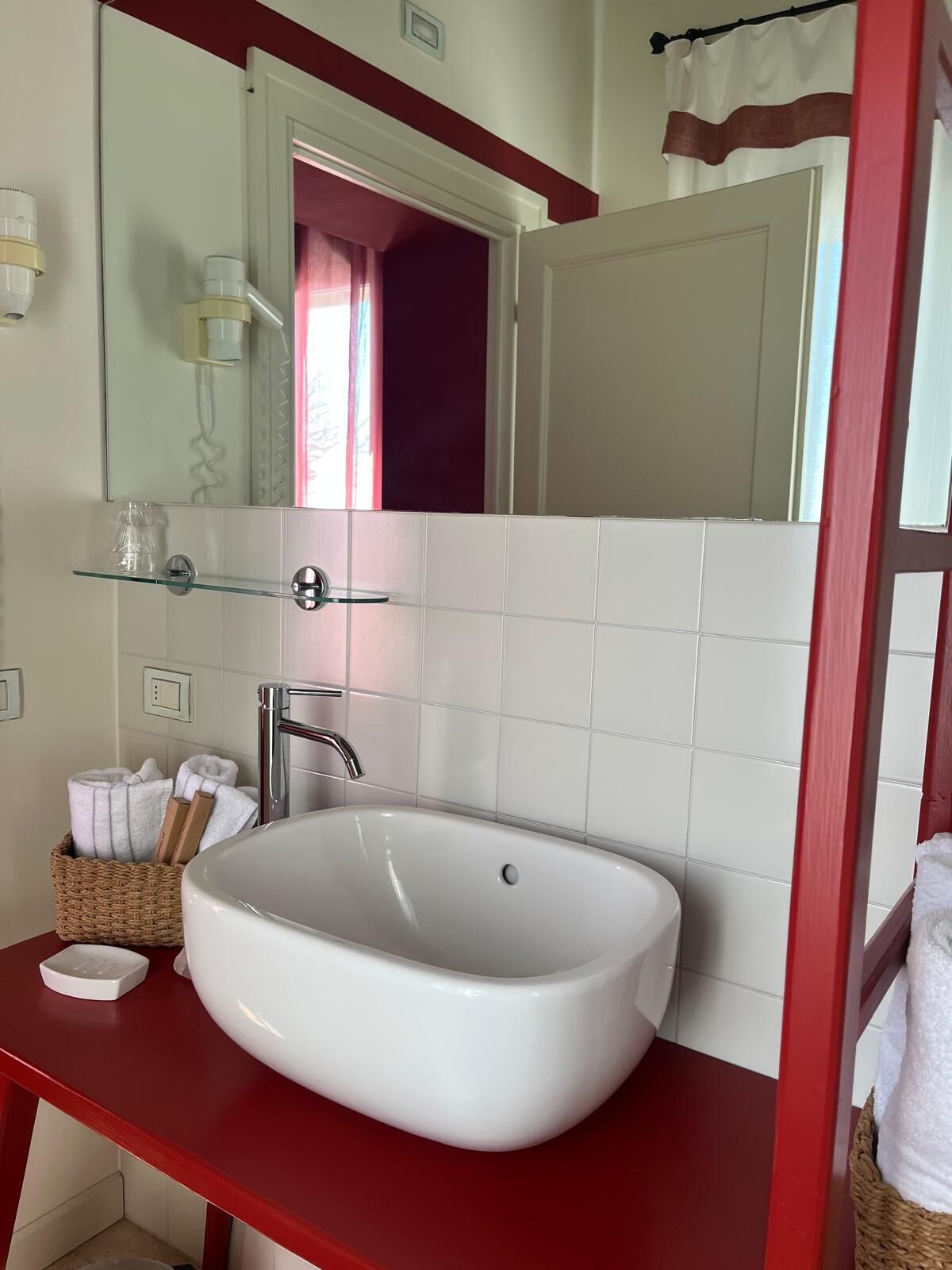 Une salle de bain avec un lavabo blanc, un plan de toilette rouge, un miroir et un porte-serviettes.