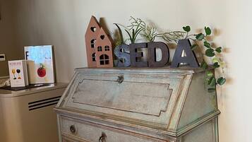 A vintage-style chest of drawers with the letters "SEDA" on top, a framed floral artwork above, and a small house-shaped decoration beside it.