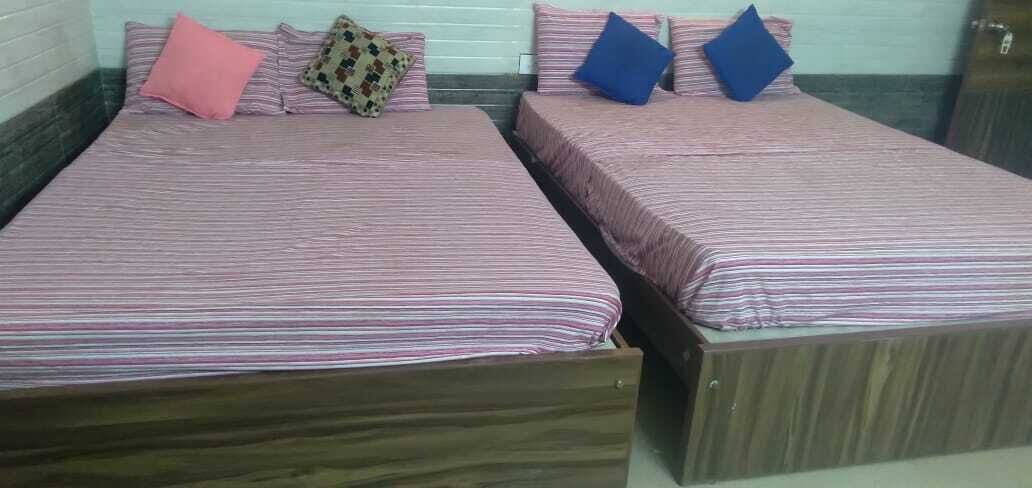 Dos camas individuales con ropa de cama a rayas y almohadas, cabeceros de madera y una pared de fondo blanca.