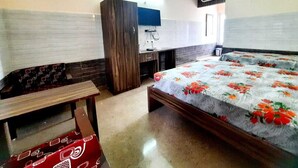 A bedroom with a bed, a bench, a wardrobe, a desk, and an air conditioning unit.