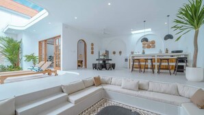 A modern living room with a large sectional sofa, a coffee table, and a dining area with a kitchen in the background. - Villa 3BR Summary:<br>VI (pererenan)