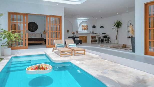 A modern indoor pool area with lounge chairs, a dining area, and a kitchen visible through an open door. - Villa 3BR Summary:<br>VI (pererenan)