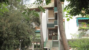Un edificio con una escalera central, un espacio exterior cubierto y un árbol en primer plano.