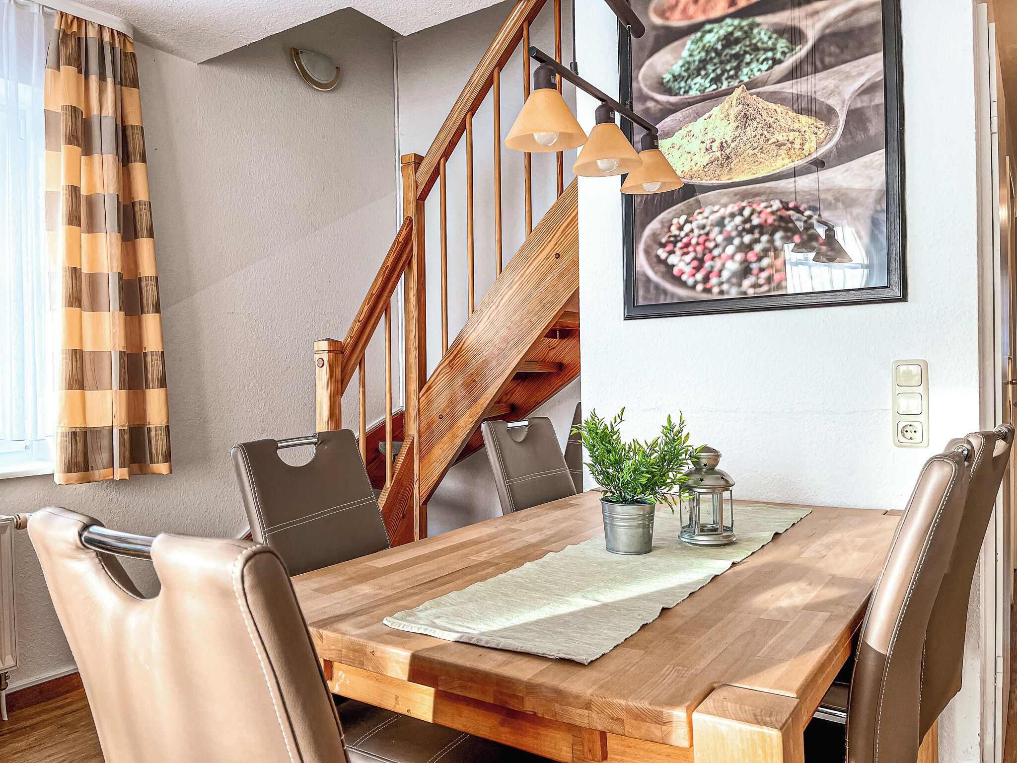 A dining area with a wooden table, leather chairs, a potted plant, and a staircase.