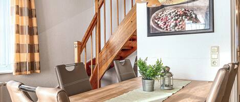 A dining area with a wooden table, leather chairs, a potted plant, and a staircase.