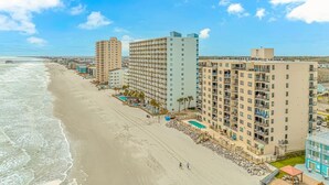 Un hotel frente a la playa con varios edificios de gran altura, una playa de arena y un cielo azul despejado.