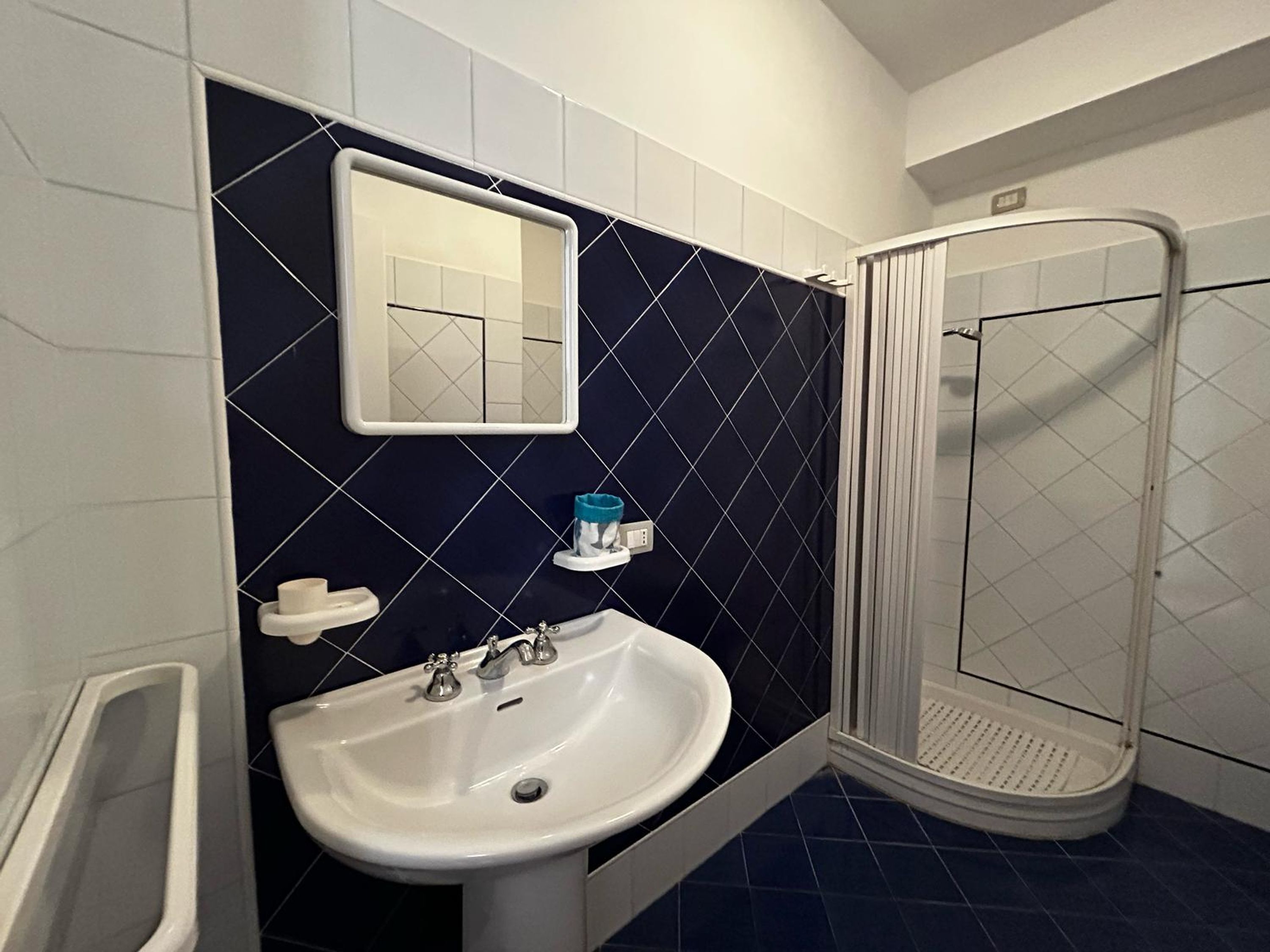A bathroom with a white sink, a mirror, a towel holder, and a shower enclosure.