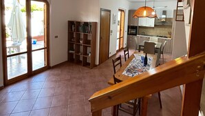 A spacious living area with a dining table, chairs, and a bookshelf. A kitchen is visible in the background. - Sogno di Mare in Marina di Ragusa (Ragusa)
