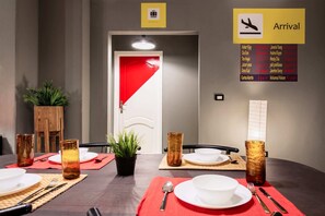Een hotelkamer met een eettafel gedekt voor vier personen, een rode deur en een aankomertafel met namen en landen.