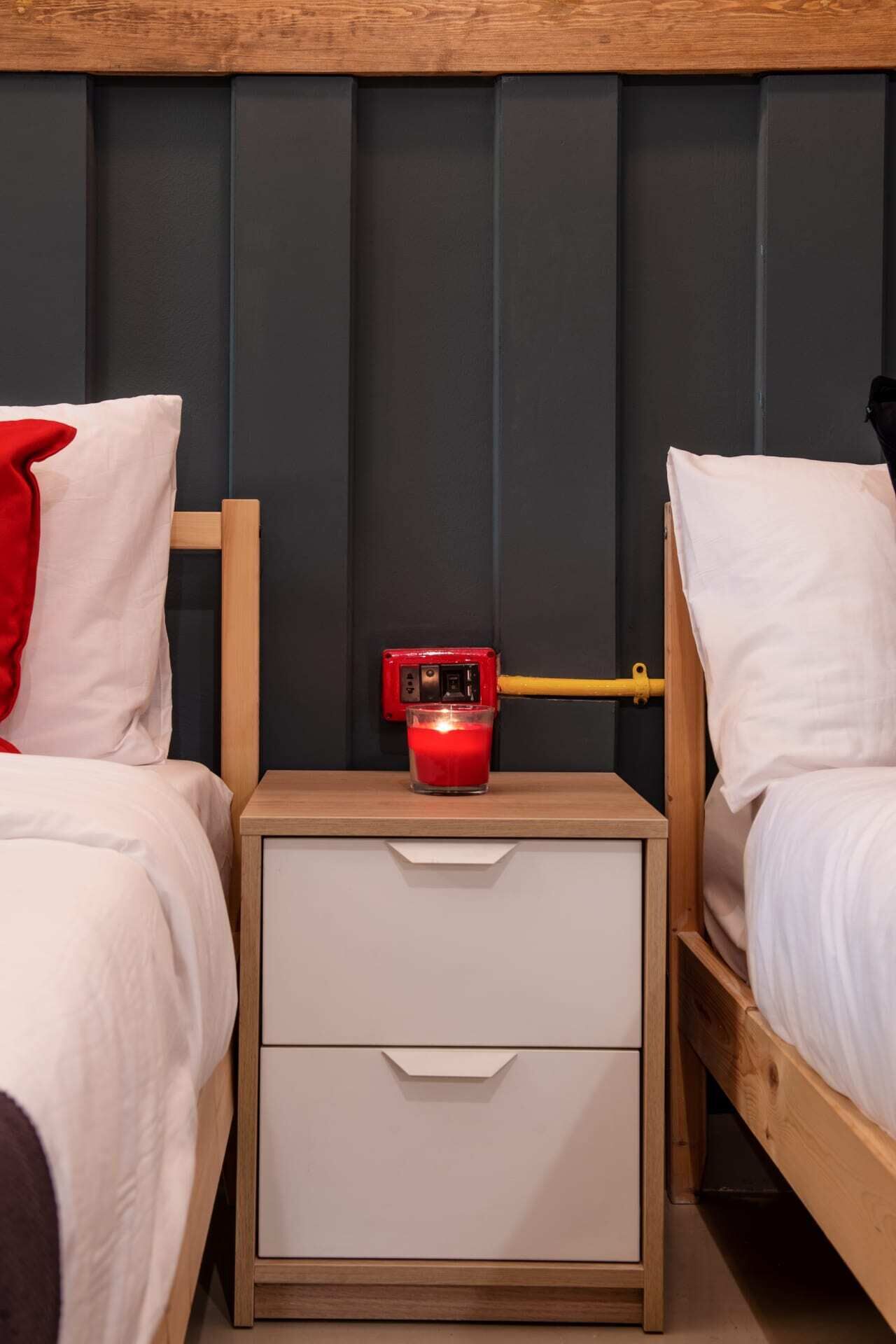 A bedroom with two beds, a nightstand with a red device, and a wooden headboard.