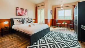 A bedroom with a bed, bedside tables, a patterned rug, a desk with chairs, and a wardrobe. - Xuru Stays I Heliopolis Rock (Cairo)