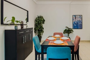A dining area with a black table, blue chairs, and a black cabinet. There are potted plants on the table and a large plant next to the cabinet.