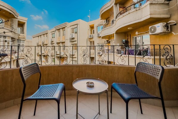 Een balkon met twee stoelen en een klein tafeltje, omgeven door een decoratieve metalen hek.