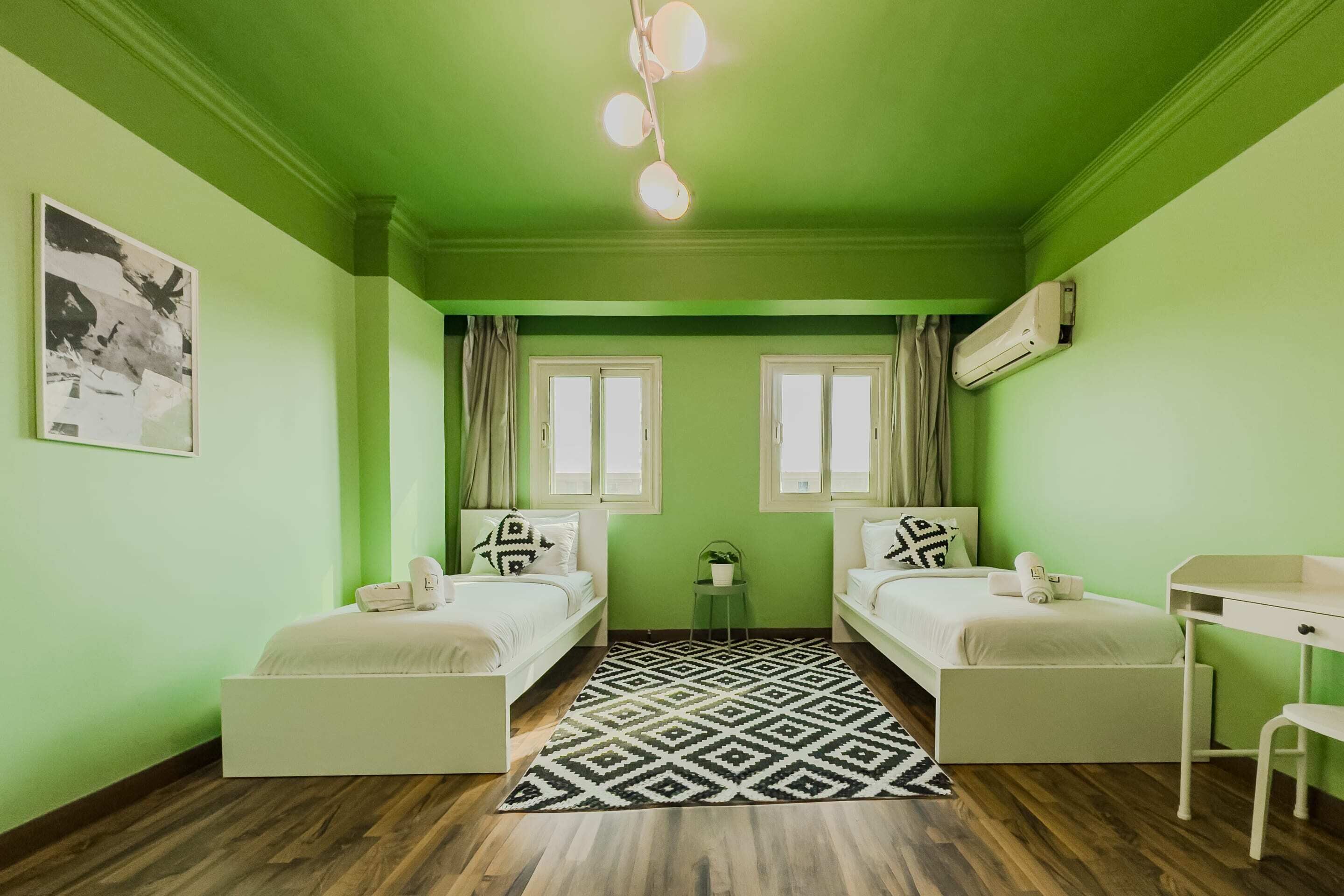 A room with two beds, a desk, a chair, a patterned rug, and a ceiling light fixture.