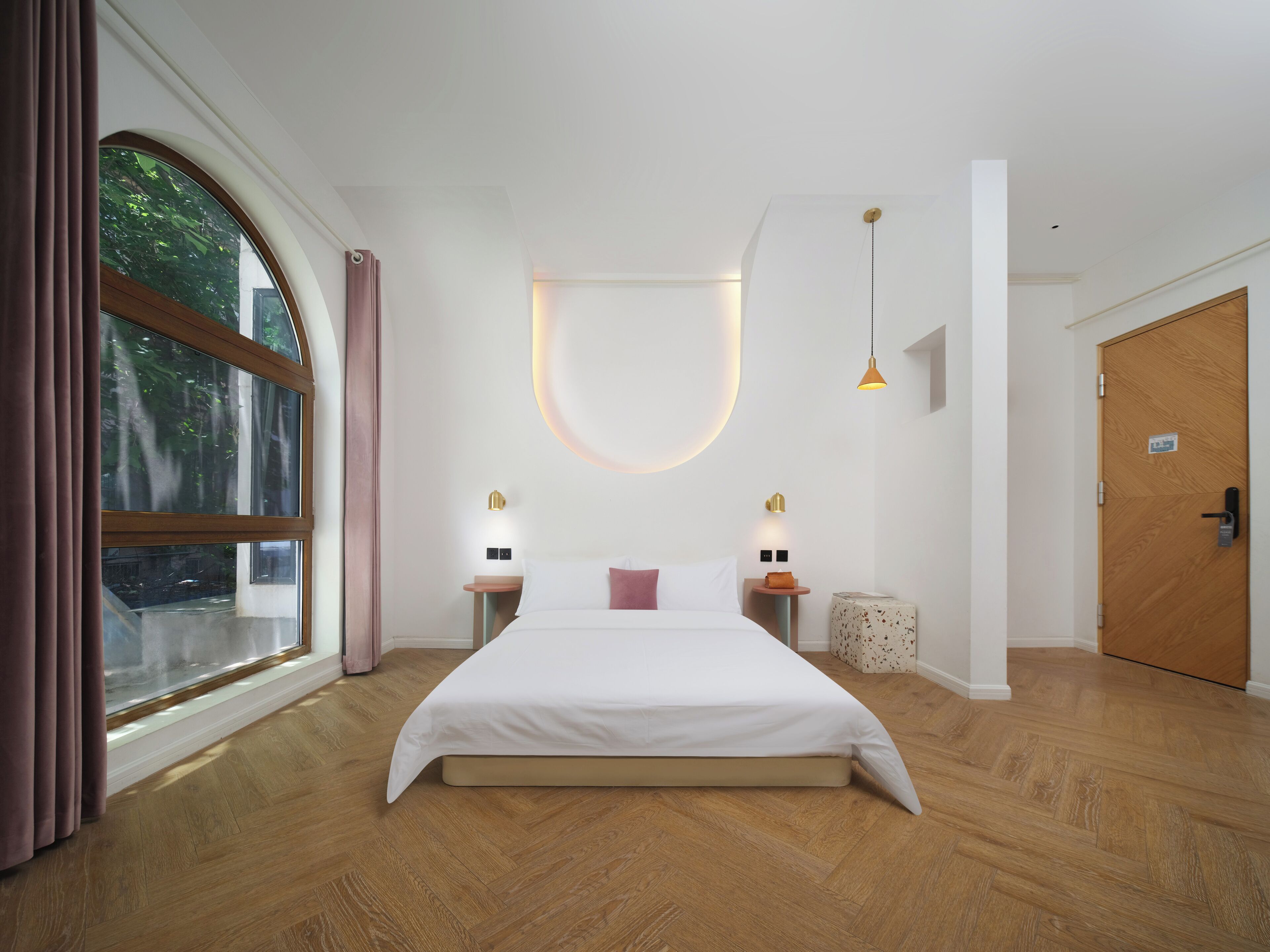 A modern bedroom with a large bed, wooden flooring, a large window with curtains, and two bedside lamps.