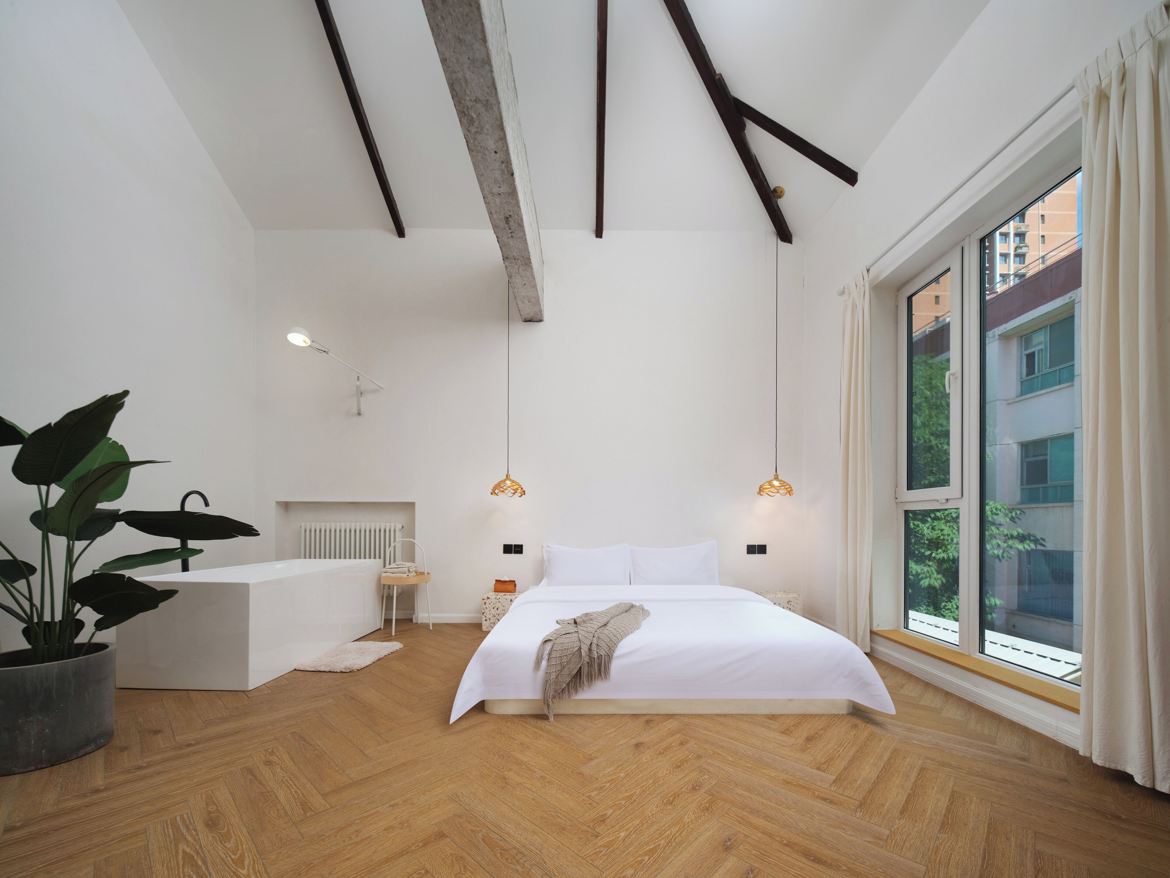 A modern bedroom with a large bed, wooden flooring, and a view of buildings through a large window.