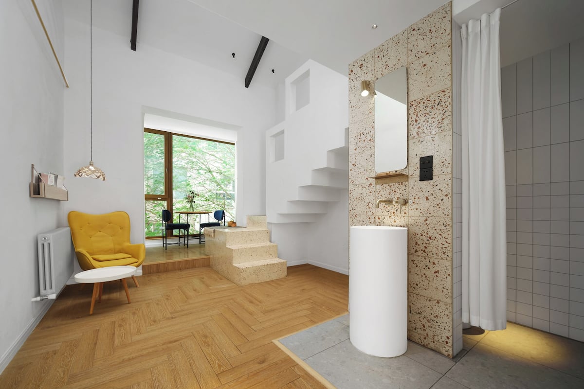 A modern interior with a wooden floor, a yellow chair, a white column, and a staircase.