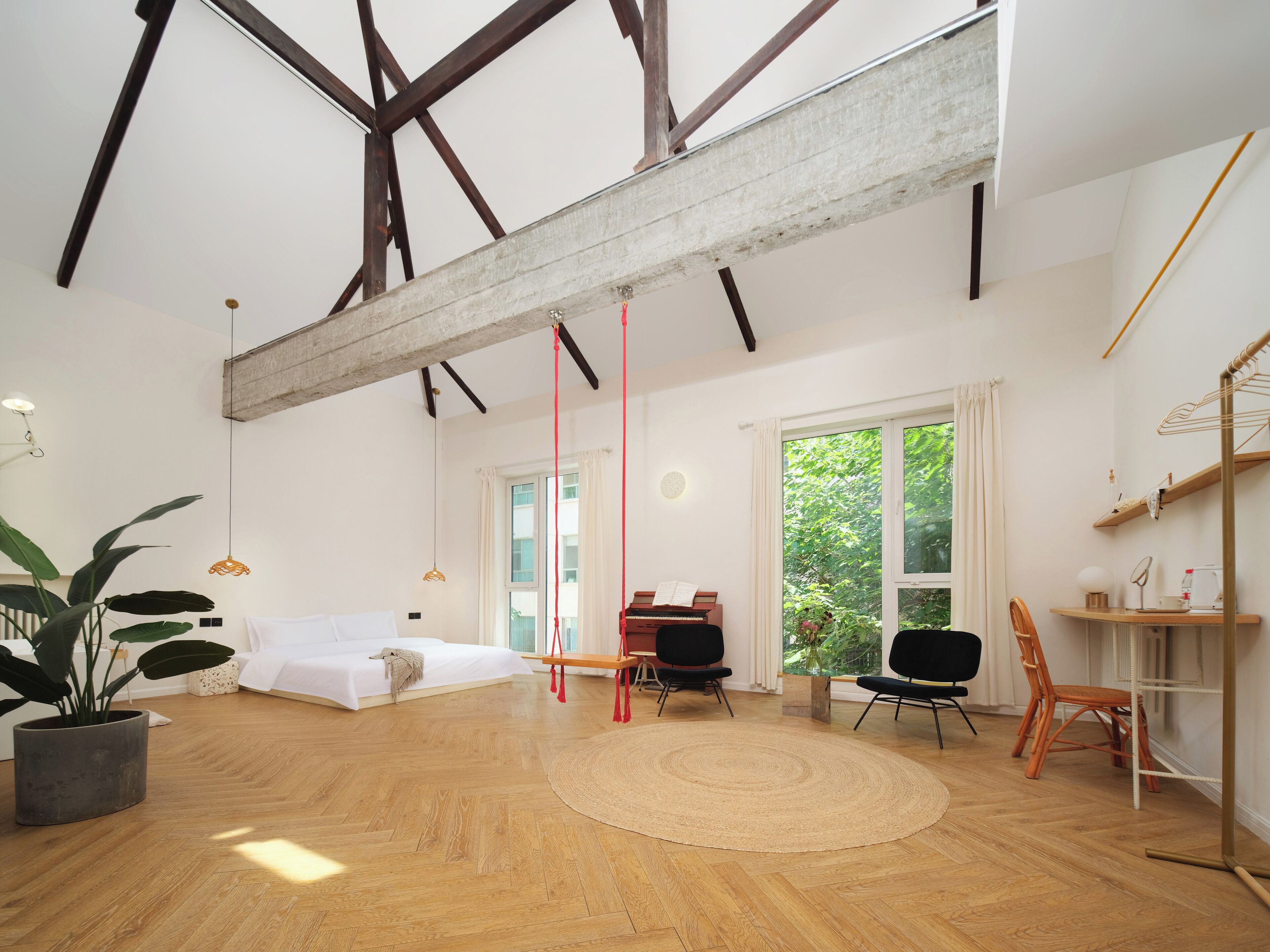 Una habitación amplia con suelo de madera, una cama, un piano y un ventanal con vistas a zonas verdes.