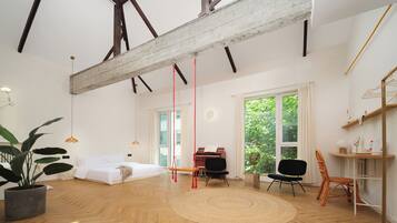 Una habitación amplia con suelo de madera, una cama, un piano y un ventanal con vistas a zonas verdes.