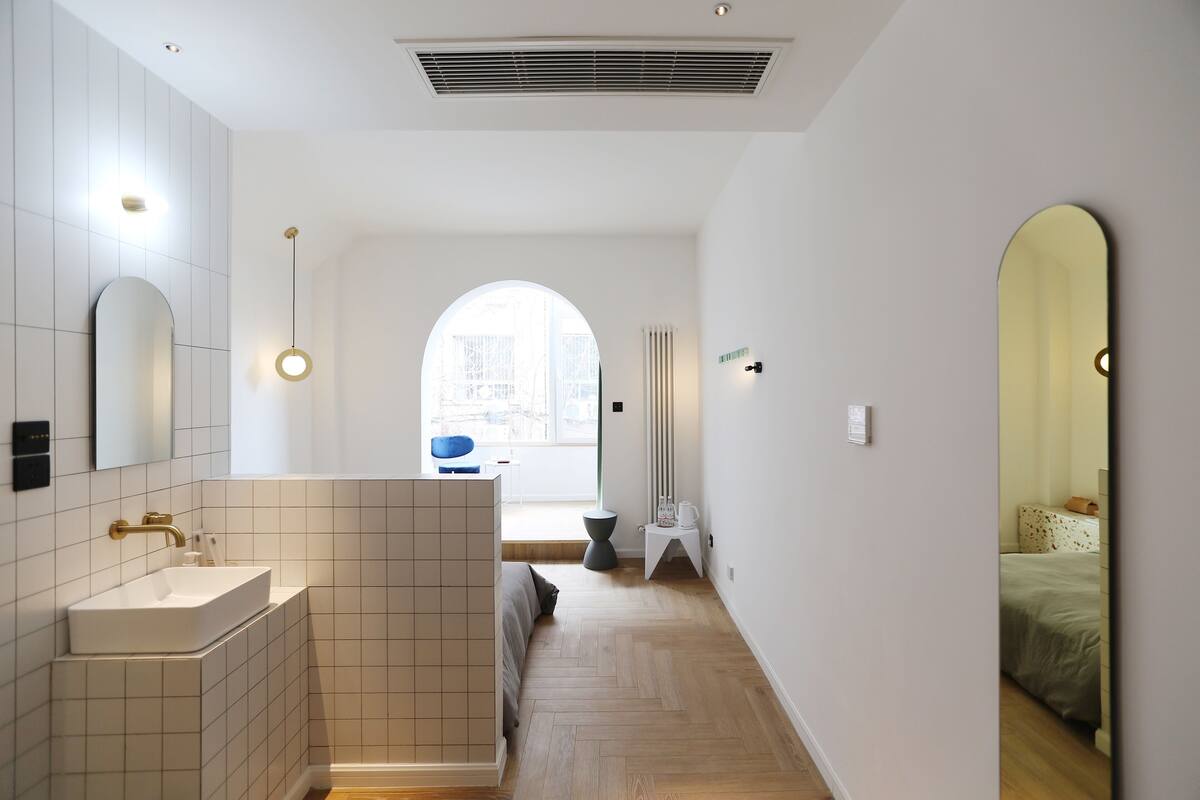 A modern bathroom with a large mirror, a white sink, and a herringbone wood floor.