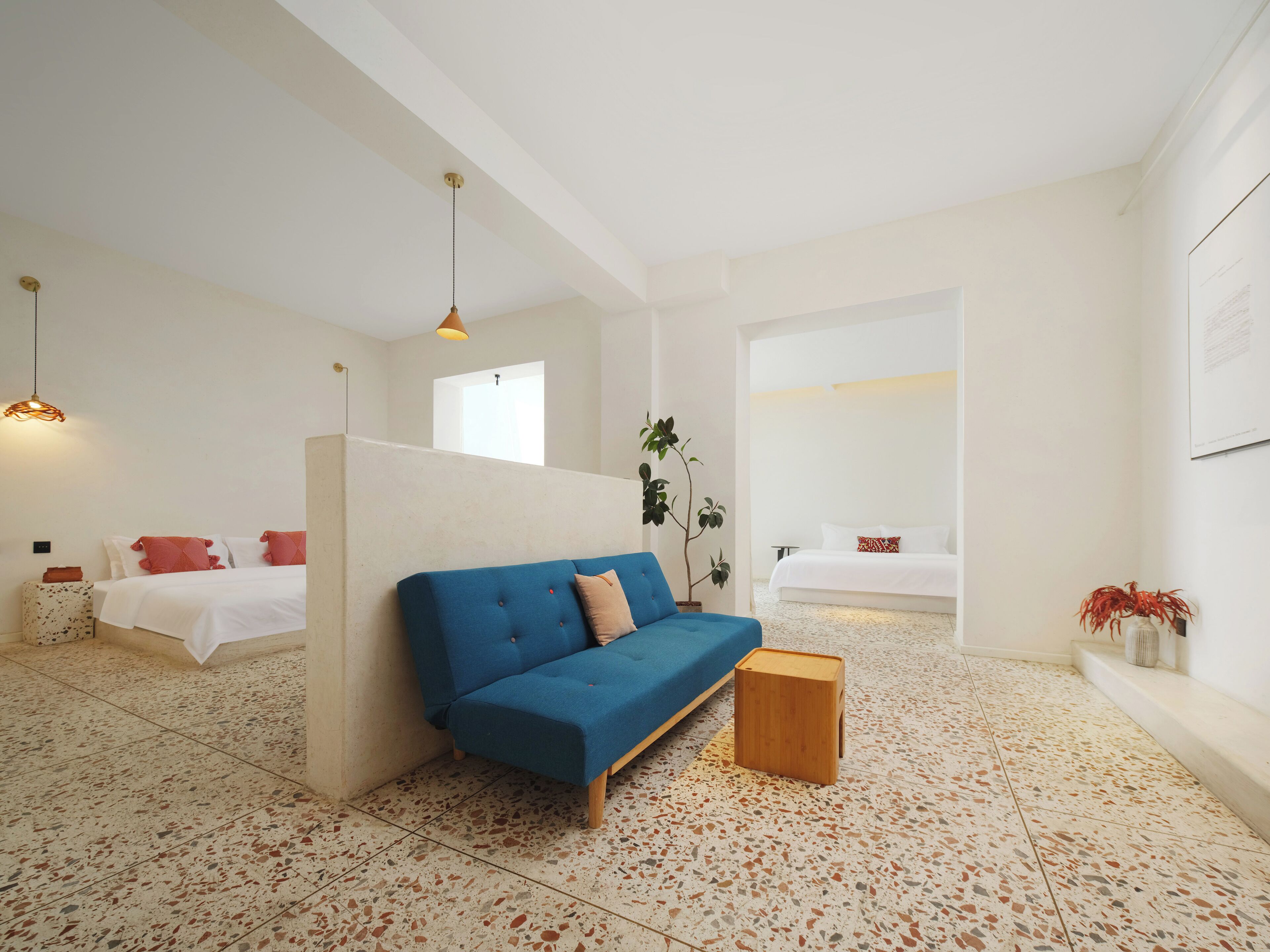 A modern hotel room with a blue sofa, a small wooden side table, and a bed with white bedding.