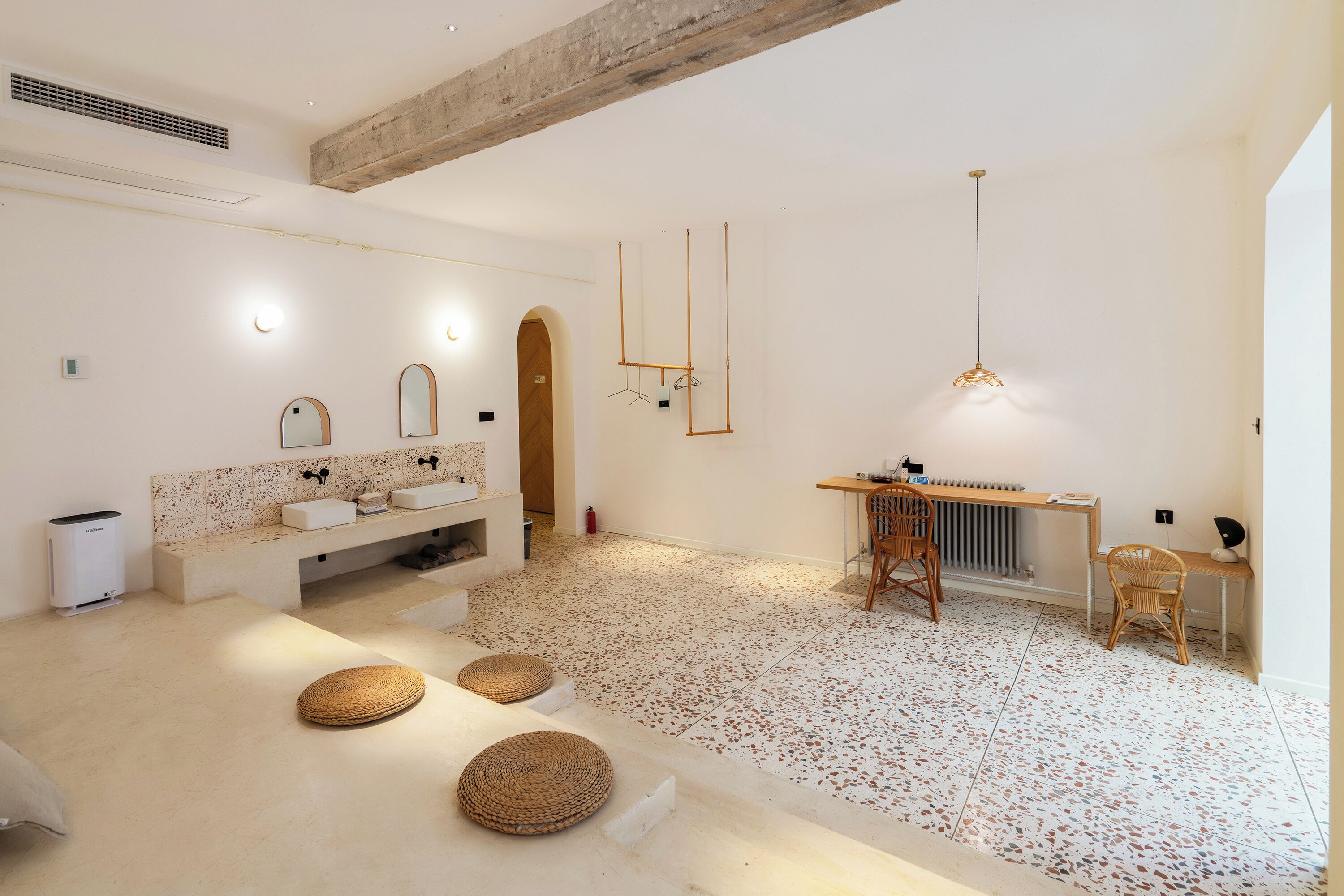 A modern bathroom with a large mirror, two sinks, a wooden bench, and a hanging light fixture.