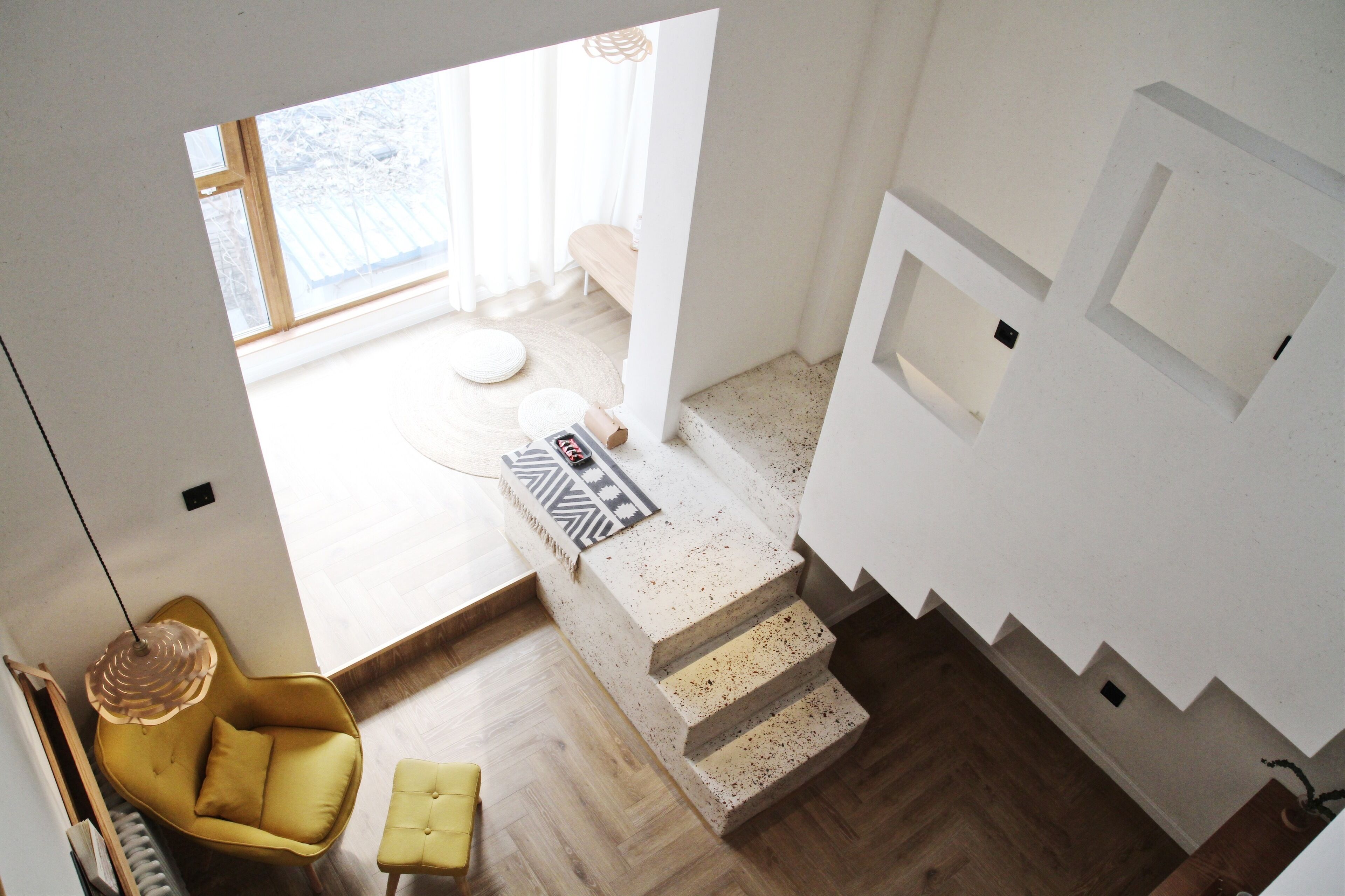 A modern interior with a staircase, a yellow chair, and a view of a room with a bed and a window.