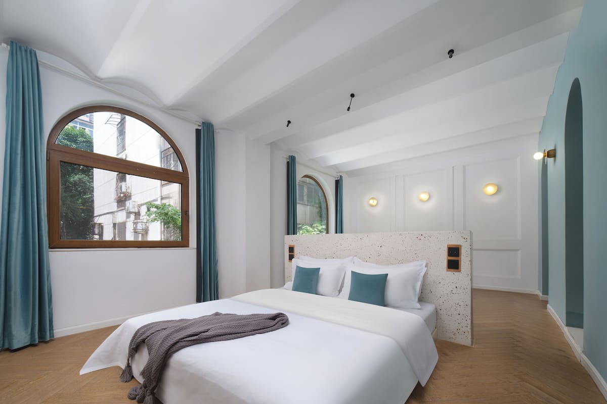 A modern hotel room with a large bed, a window with curtains, and a view of the city.