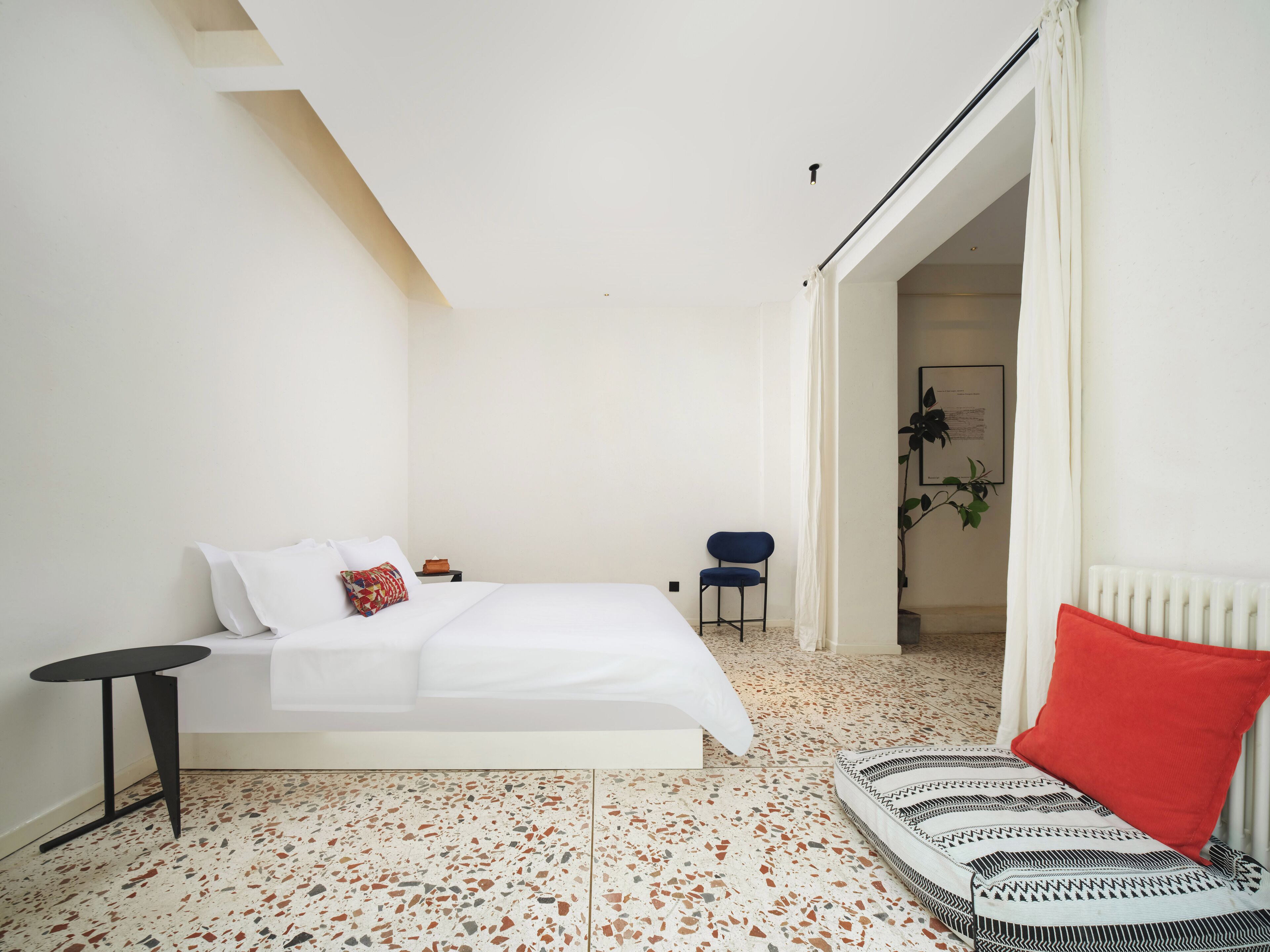 A bedroom with a bed, a small table, a chair, and a radiator.
