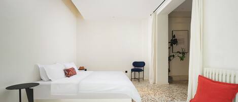 A bedroom with a bed, a small table, a chair, and a radiator.