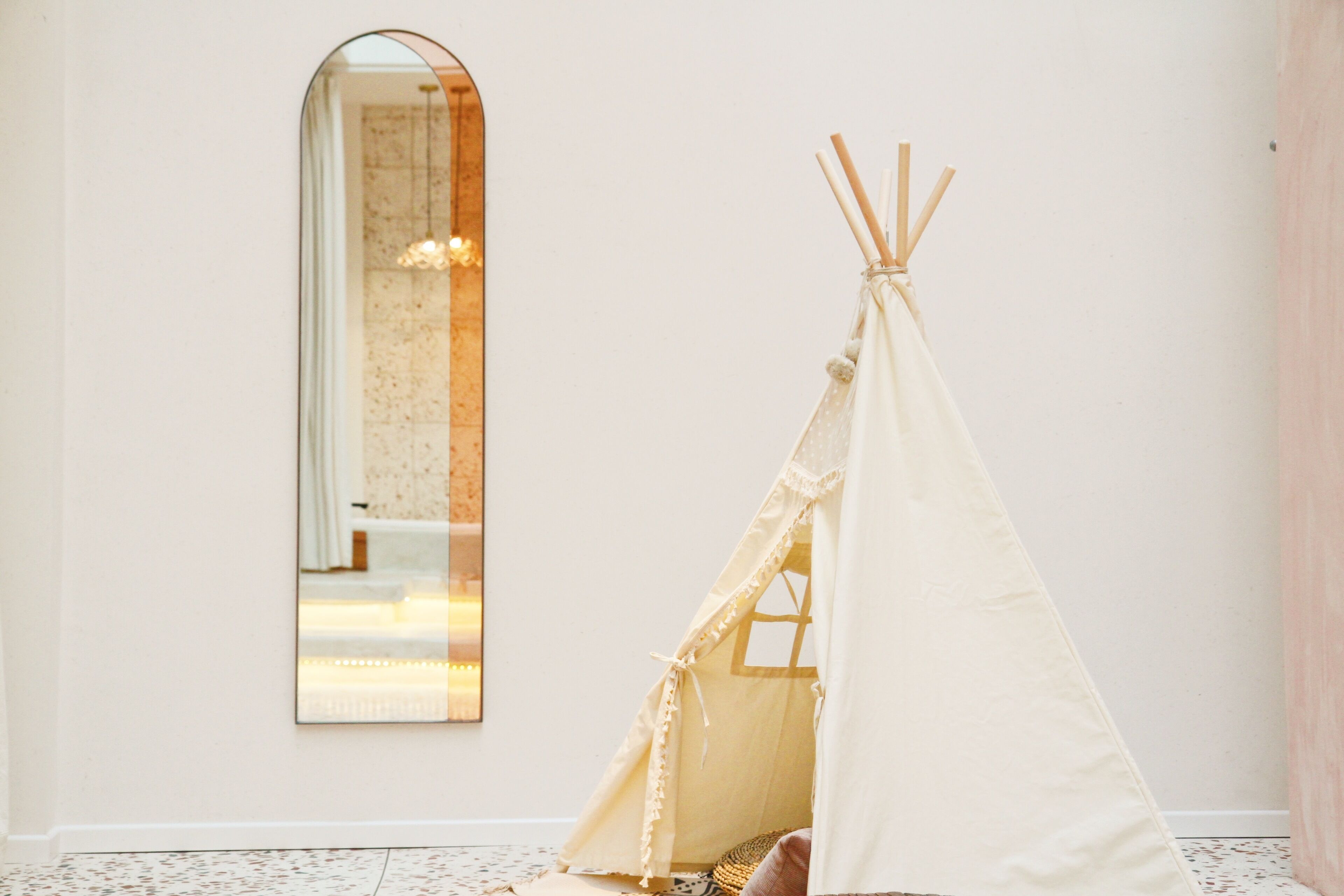 A room with a white wall, a large mirror, and a white teepee-like structure.