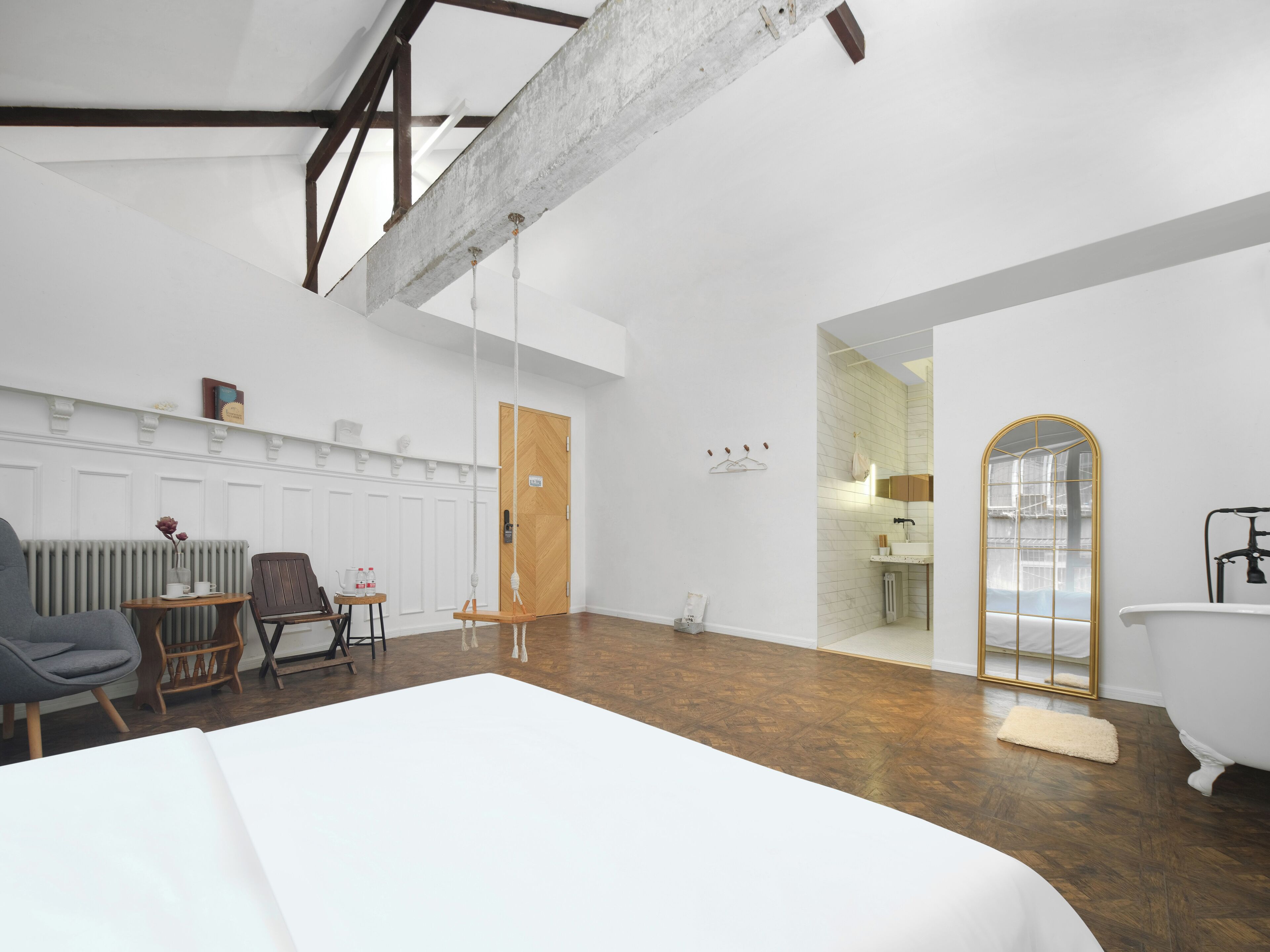 A spacious room with a large bed, a wooden floor, a radiator, a wooden door, and a bathroom with a bathtub and mirror.