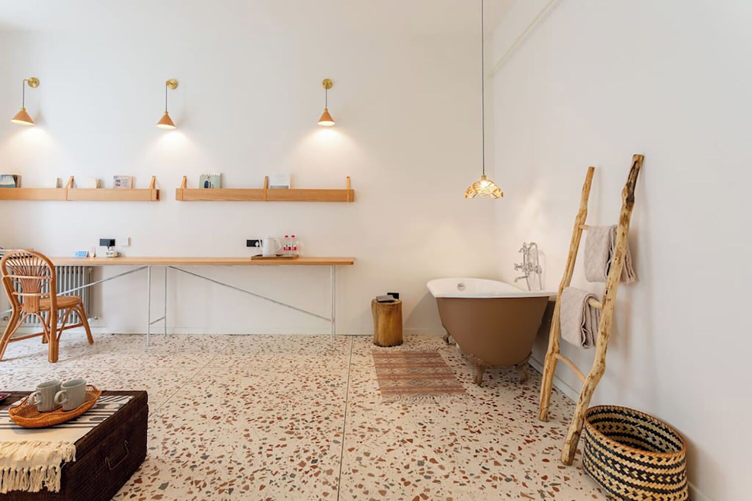 Une salle de bain avec une baignoire sur pieds, une chaise en bois, une petite table avec des tasses et une étagère contenant des articles de toilette.