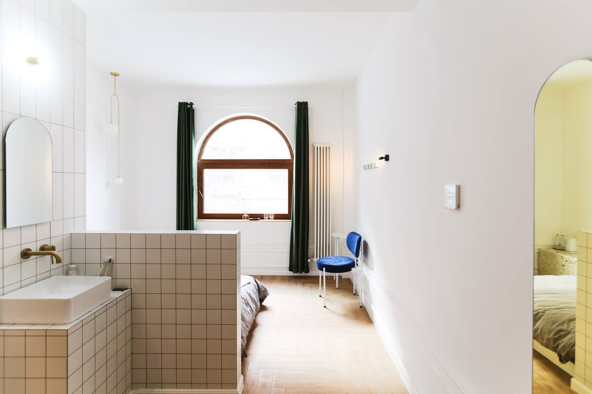 A modern bathroom with a white sink, a shower, and a window with curtains.