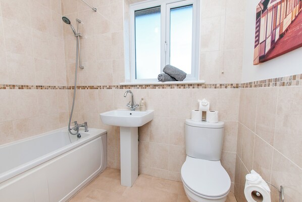 Un baño con bañera, lavamanos, inodoro y una ventana sobre el inodoro.