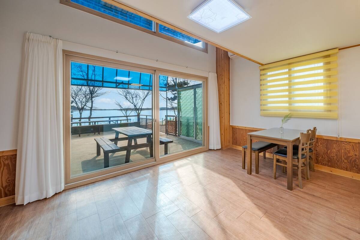 A spacious room with a sliding glass door leading to an outdoor patio area, a wooden dining table, and a kitchen area with a sink.