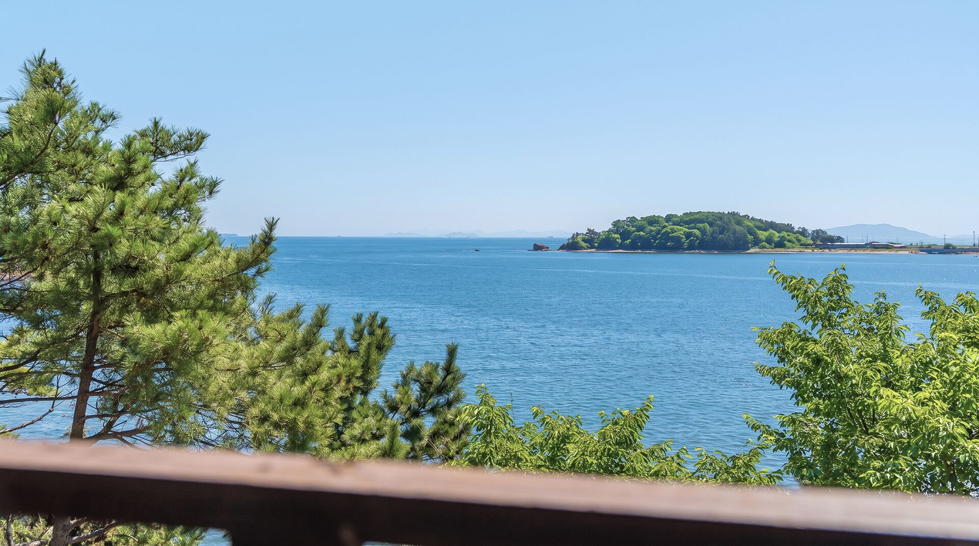 Une vue sur la côte, avec un ciel dégagé, une étendue d’eau et une île au loin.