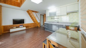A modern kitchen with a built-in stove, a dining area with a glass table, and a wooden staircase leading to a loft bedroom. - Yeongheungdo Rainbow Ocean View Pension (Incheon)