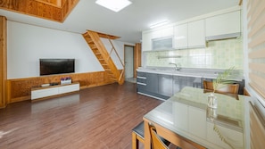 Une cuisine moderne dotée d’une cuisinière intégrée, un coin repas avec une table en verre et un escalier en bois menant à une chambre en mezzanine.