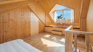 A wooden attic bedroom with a sloped ceiling, a large window, and a bench with two chairs. - Yeongheungdo Rainbow Ocean View Pension (Incheon)